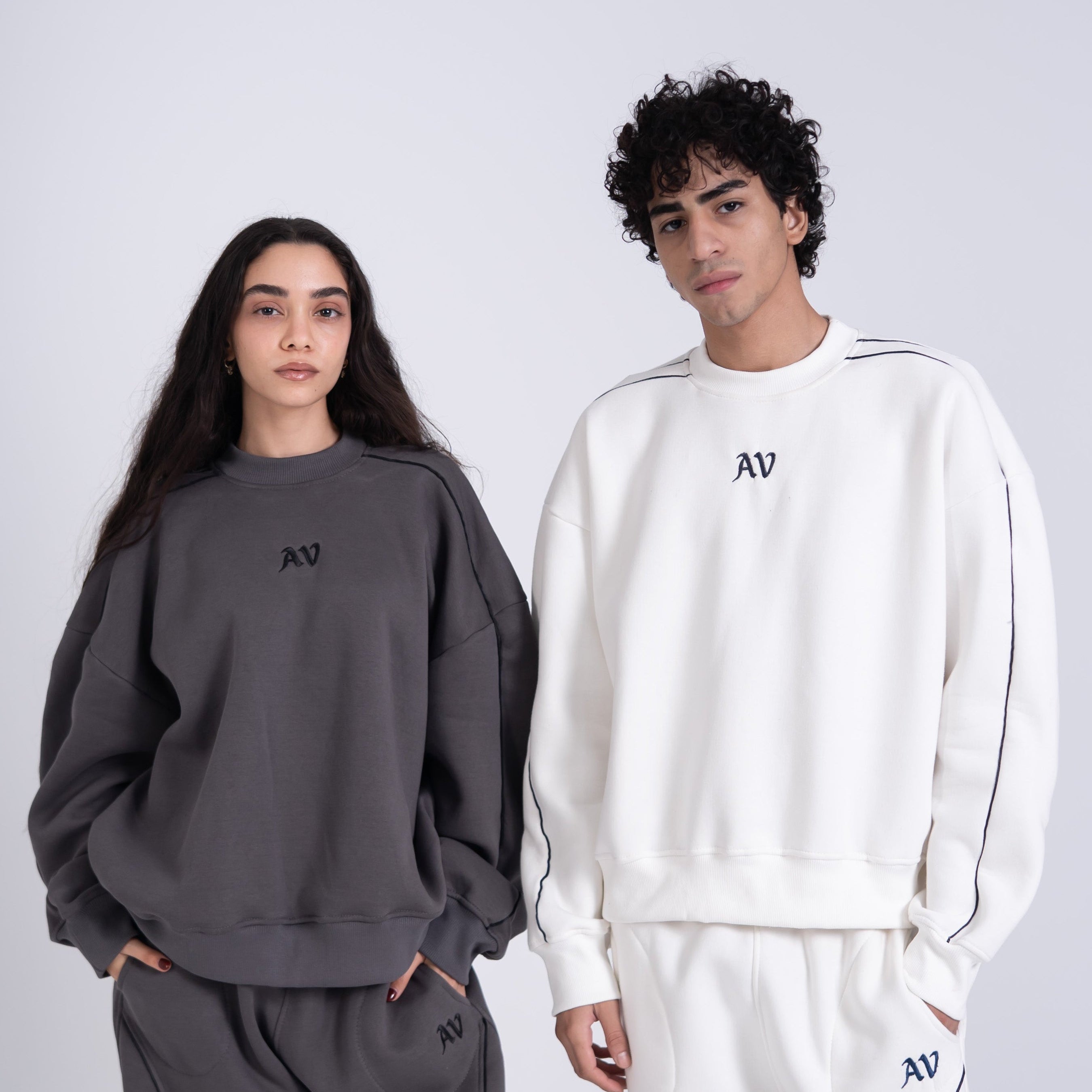 Two people wearing matching gray and white tracksuits on a plain background